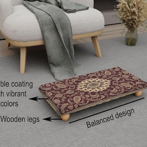 May include: A rectangular footstool with a burgundy floral pattern and a beige border. The footstool has a durable coating and is supported by four wooden legs. The text on the image says "Durable coating with vibrant colors" and "Wooden legs".