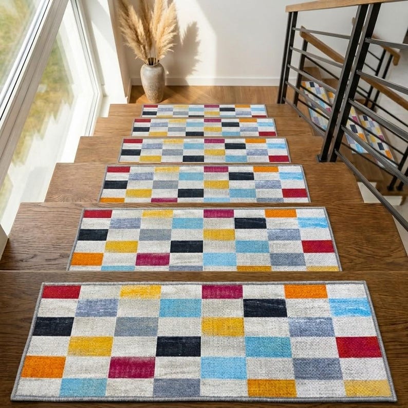 a set of three colorful, geometric-patterned rugs arranged on a wooden floor, with a staircase visible in the background.