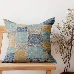 May include: A blue, yellow, and gray patterned throw pillow with a patchwork design. The pillow is sitting on a wooden chair.