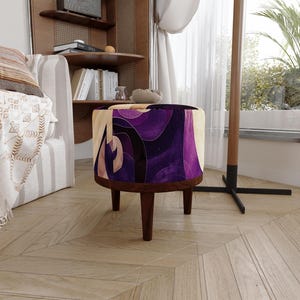 May include: A round ottoman featuring a vibrant purple and cream abstract wave pattern on its upholstered top. The base is constructed from dark brown wood and is supported by four short, tapered wooden legs that provide a stable foundation.
