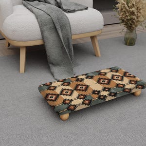 May include: A rectangular footstool with a patterned design in shades of brown, tan, and teal. The footstool has a wooden frame and four short, rounded legs. The design features geometric shapes and patterns.