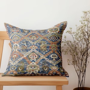 Peut inclure: Un coussin de décoration bleu et orange à motifs géométriques. Le coussin est posé sur une chaise en bois.