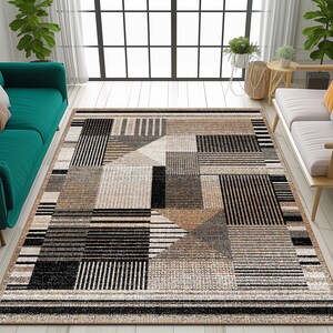 Op de afbeelding: Een geometrisch patroon tapijt met zwarte, bruine en beige strepen en vierkanten. Het tapijt ligt op een lichte houten vloer in een woonkamer.