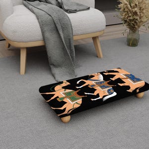 May include: A rectangular footstool featuring a black background with a vibrant illustration of horses and riders. The horses are tan with white manes and tails, and the riders wear green and blue attire. The stool has four wooden legs.