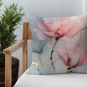May include: A decorative throw pillow with a floral design. The pillow features two pink flowers with gold accents on a light blue background.