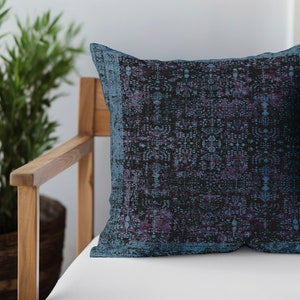 Könnte beinhalten: Ein blaues und violettes Kissen mit geometrischem Muster. Das Kissen liegt auf einem Holzstuhl mit einem weißen Kissen.