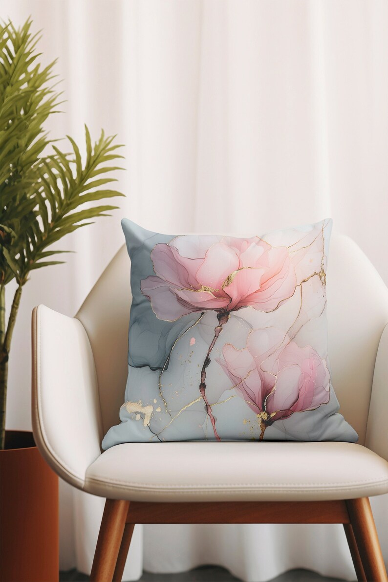 May include: A decorative throw pillow with a watercolor-style design of pink flowers with gold accents on a light blue background.