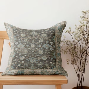 Könnte beinhalten: Ein dekoratives Kissen mit einem grauen und blauen Blumenmuster. Das Kissen liegt auf einem Holzstuhl.