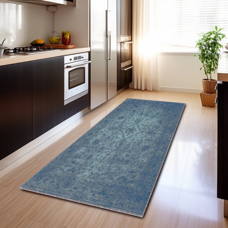 May include: A blue and green distressed runner rug with a faded floral pattern. The rug is placed in a kitchen with hardwood floors.