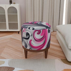 May include: A round, pink, black, and white patterned ottoman with wooden legs. The ottoman is sitting on a wood floor.