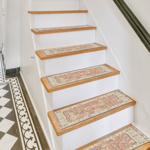 May include: A set of six patterned stair treads in a beige, pink, and cream color scheme. The treads are placed on a set of wooden stairs with a white painted riser.
