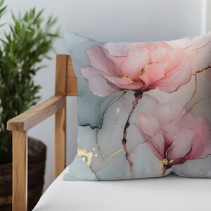 May include: A decorative throw pillow with a floral design. The pillow features two pink flowers with gold accents on a light blue background.