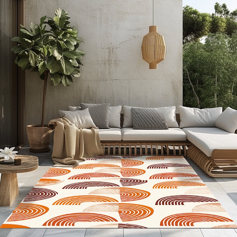 May include: A white area rug with a geometric pattern of orange and brown semi-circles. The rug is laid out on a patio with a white couch and a potted plant.