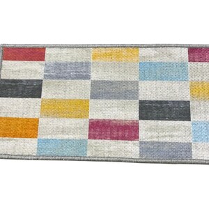 a colorful rug with a geometric pattern of squares in various shades of gray, yellow, orange, and pink.