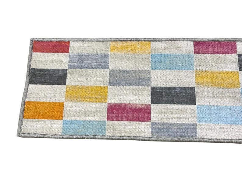 a colorful rug with a geometric pattern of squares in various shades of gray, yellow, orange, and pink.