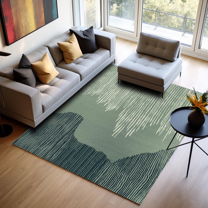 May include: A green and blue patterned area rug with a contemporary design. The rug is laid out in a living room with a gray sofa and a gray armchair.