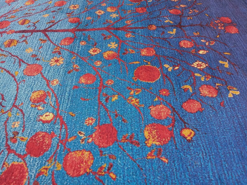 May include: A blue rug with a repeating pattern of a tree with red pomegranates and small yellow flowers.