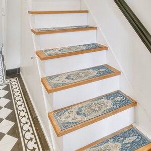 Puede incluir: Escalera con contrahuellas blancas y pelda&ntilde;os de madera. Cada pelda&ntilde;o presenta una alfombra rectangular con un patr&oacute;n ornamental azul, beige y marr&oacute;n. La escalera tiene una barandilla negra y est&aacute; en un interior bien iluminado.