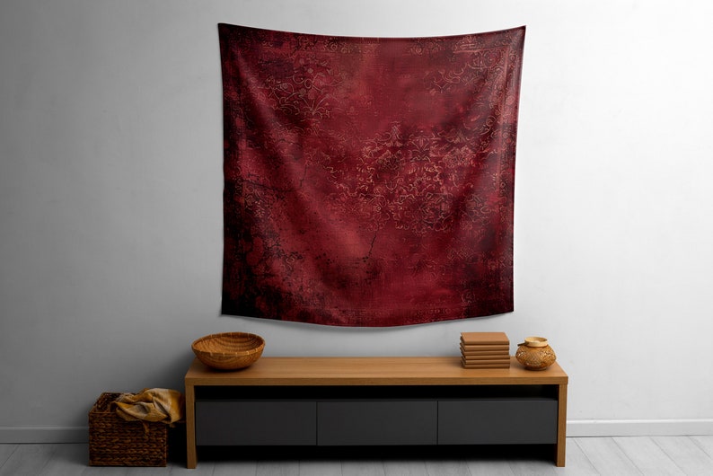 May include: A red tapestry with a distressed, vintage look hangs on a white wall above a wooden shelf with a bowl and books.