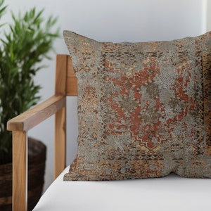 May include: A decorative throw pillow with a distressed, vintage-inspired pattern in shades of brown, red, and gold. The pillow is sitting on a wooden chair with a white cushion.