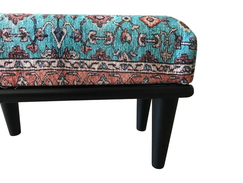 A colorful, patterned ottoman or footstool with a teal and orange color scheme, placed on a black wooden frame.