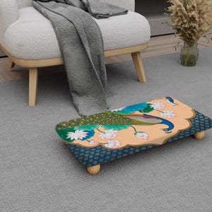 May include: A decorative footstool with a peacock design. The stool has a light orange background with a peacock illustration in blue, green, and gold. The edges are dark blue with a gold pattern, and it has four wooden legs.