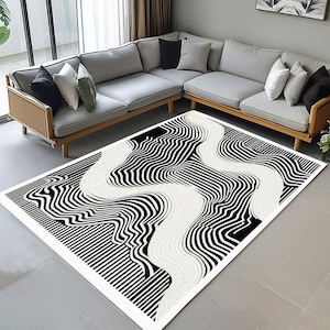 May include: Black and white abstract area rug with a wavy, striped pattern. The rug is on a gray tiled floor in front of a gray couch.