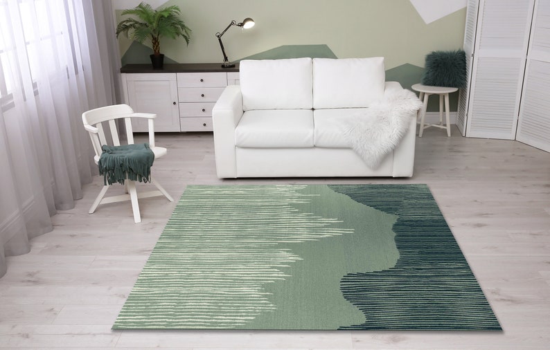 May include: A green and blue abstract patterned area rug with a white sofa and a white chair in the background.