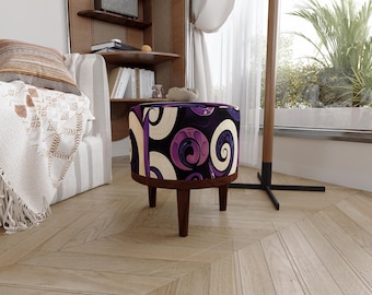 May include: A round ottoman featuring a dark purple and cream-coloured fabric with a swirling, abstract pattern. The piece is supported by four short, tapered wooden legs with a dark brown finish, providing a stable base for the upholstered seat.
