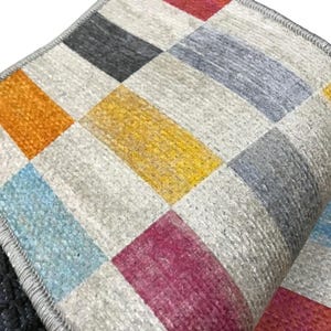 a close-up view of a colorful, geometric patterned rug or carpet with a mix of gray, orange, yellow, and pink squares.