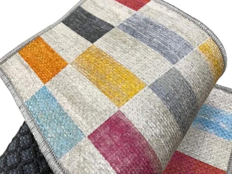 a close-up view of a colorful, geometric patterned rug or carpet with a mix of gray, orange, yellow, and pink squares.