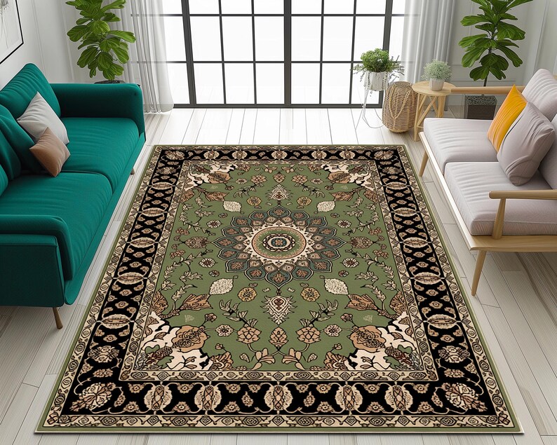 a living room with a large, ornate rug in the center. The rug has a floral design and is surrounded by two couches, one green and one white. The room also features a large window, a wooden side table, and several potted plants.