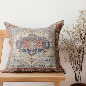 Puede incluir: Una almohada decorativa con un dise&ntilde;o estampado en azul, rojo y beige. La almohada est&aacute; sentada en una silla de madera.