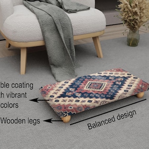 May include: A rectangular footstool with a patterned design in shades of blue, red, and cream. It features a durable coating and wooden legs. The design is balanced, and the footstool is placed on a gray rug.