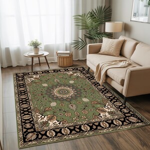 a cozy living room with a large, ornate rug featuring a floral design in shades of green and black. The rug is placed on a wooden floor, and a beige sofa is positioned against the wall. A small table with a plant and a lamp is located next to the sofa, and a window with white curtains allows natural light to enter the room.