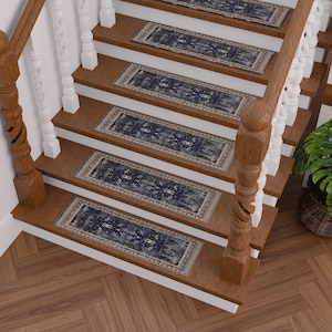 Puede incluir: Un conjunto de cinco peldaños de escalera con estampado azul y crema con un borde decorativo. Los peldaños están colocados en una escalera de madera con una barandilla blanca.