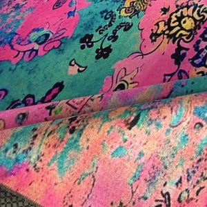 a vibrant, colorful fabric with a pattern of flowers and abstract shapes in various shades of pink, blue, green, and yellow.