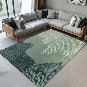 May include: A green and blue abstract area rug with a striped pattern. The rug is laid out on a light gray tiled floor in front of a gray sectional sofa.