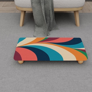 May include: A rectangular wooden footstool with a colorful retro design. The top features a pattern of flowing lines in shades of orange, blue, cream, and red. It has four small, round wooden legs.