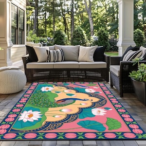 May include: A colorful outdoor rug featuring a peacock design with lotus flowers and leaves. The rug has a pink background with a blue border and is placed on a patio with outdoor furniture.