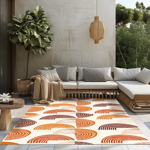 May include: A white area rug with a geometric pattern of orange and brown semi-circles. The rug is laid out on a patio with a white couch and a potted plant.