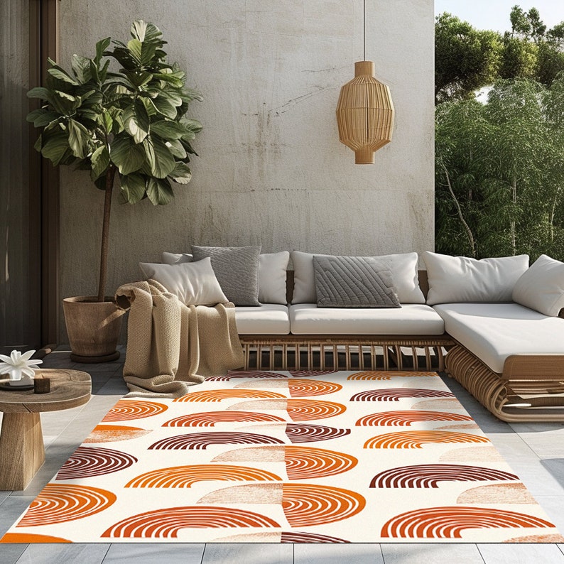 May include: A white area rug with a geometric pattern of orange and brown semi-circles. The rug is laid out on a patio with a white couch and a potted plant.