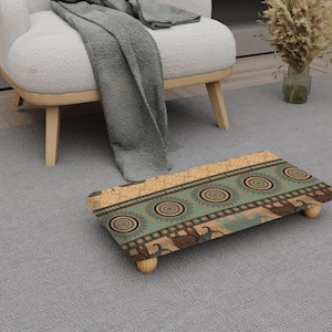 May include: A patterned footstool in teal, brown, and beige. The rectangular stool has a design featuring circular and floral motifs. It is supported by four small wooden legs. The footstool is a decorative item for the home.