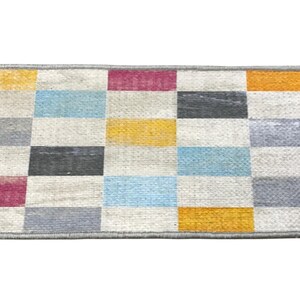 a colorful rug with a geometric pattern of squares in various shades of gray, yellow, orange, and pink.