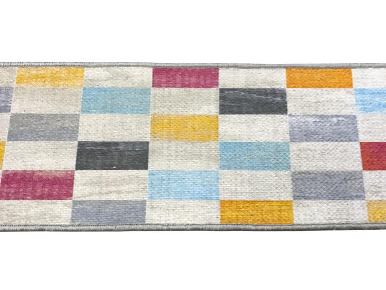a colorful rug with a geometric pattern of squares in various shades of gray, yellow, orange, and pink.