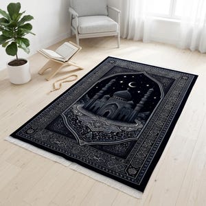 May include: A black prayer rug featuring a mosque design with a night sky backdrop, stars, and a crescent moon. The rug has a detailed border and fringe.