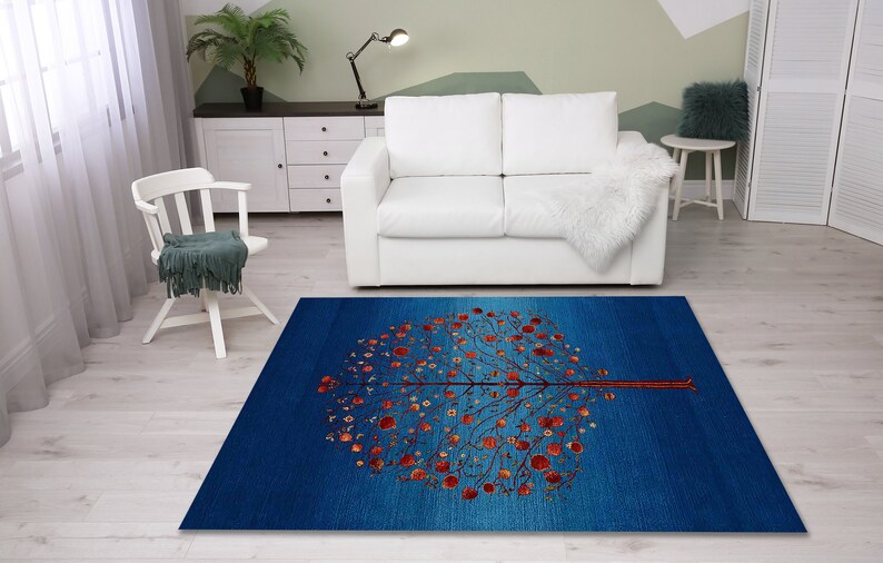 May include: A blue and red area rug with a stylized tree design. The tree has a brown trunk and branches with red leaves. The rug has a gradient design with a darker blue color at the bottom and a lighter blue color at the top.