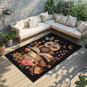 May include: A black area rug featuring a brown owl perched on a book, surrounded by flowers and butterflies. The owl has large, round eyes and a brown and white patterned body. The book is open and has a brown cover with gold accents. The flowers are pink, yellow, and orange. The butterflies are blue and purple.