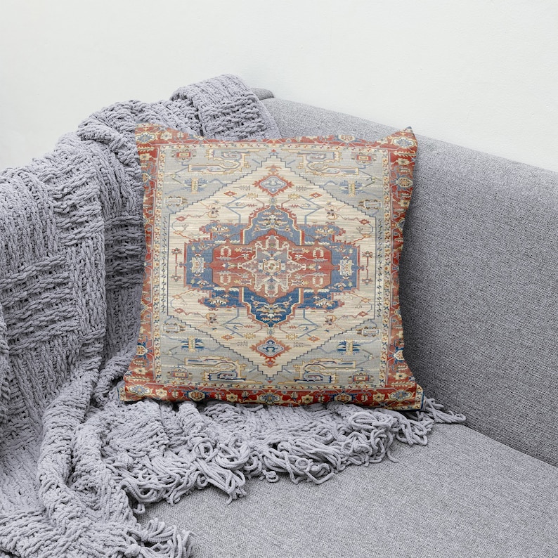 Puede incluir: Una almohada decorativa con un patr&oacute;n colorido e intrincado que recuerda a una alfombra tradicional. La almohada presenta un dise&ntilde;o central en tonos azules, rojos y beige, rodeado de un borde de formas geom&eacute;tricas.