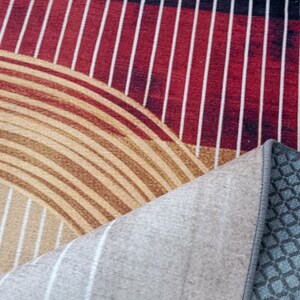May include: Close-up of a rug with a geometric pattern of red and white stripes, brown and white concentric circles, and a gray backing with a diamond pattern.